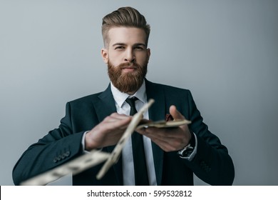 portrait of stylish businessman throwing dollar banknotes isolated on grey