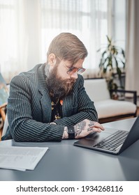 Portrait Of A Stylish Computer Programmer Wearing Custom Stylish Clothing With Sunglasses. Man Working On Laptop At Home.