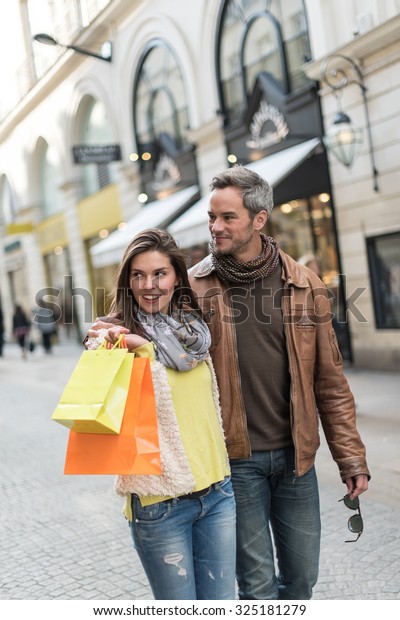 Portrait of a stylish couple doing their shopping\
in the city center The grey hair man with beard is wearing a\
leather coat and the woman a yellow top and two shopping bags, they\
also have scarfs