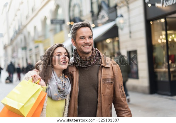 Portrait of a stylish couple doing their shopping\
in the city center The grey hair man with beard is wearing a\
leather coat and the woman a yellow top and two shopping bags, they\
also have scarfs
