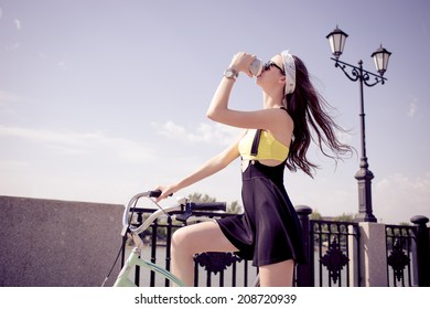 Portrait of a stylish girl hipster riding a cruiser bicycle drinking coffee from disposable cup - Powered by Shutterstock