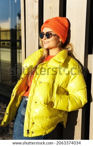 Portrait of  stylish girl wearing yellow puffer and orange knitted hat 