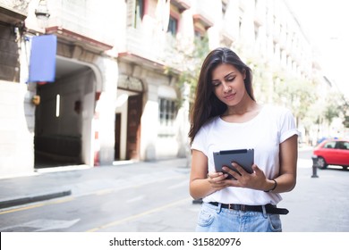 Portrait of a stylish hipster girl using her digital tablet for navigation in urban setting, attractive latin woman reading digital e-book on touch pad during walking in summer day, copy space area