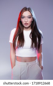 Portrait Of A Stylish Indian Woman In A White T-shirt With Transparent Glasses And With Pockets In Her Pants. Red Light In The Background