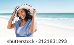 Portrait of stylish latin hispanic woman with white straw hat standing at beach. Young smiling woman on vacation enjoy sea breeze wearing straw hat and looking at camera. Attractive beautiful girl.