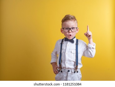 Portrait of stylish little boy with finger pointed up. Little child in glasses has idea. Kid isolated on yellow blackboard. Success, bright idea, creative ideas and innovation technology concept.