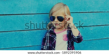Portrait of stylish little girl child posing on a blue wooden background