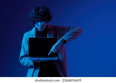 Portrait of a stylish male hacker with a laptop and futuristic glasses in blue light, Blue Perennial color, cyber security, technology and education, neon color, freelancer online work, trend color