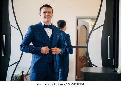 Portrait of a stylish man in a business suit in a wide cage. The young man wore trousers, a shirt, a waistcoat and a bow-tie, and buttoned his jacket. He looks in the mirror when he is dressing - Powered by Shutterstock