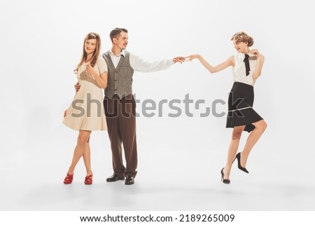 Portrait of stylish man in retro suit flirting with two beautiful women isolated over white studio background. Party communication. Concept of retro fashion, style, youth culture, emotions, beauty, ad