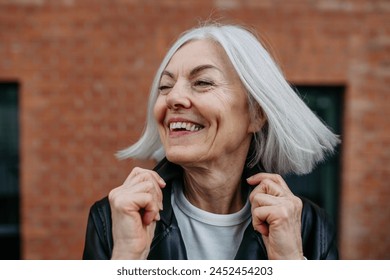 Portrait of stylish mature woman with gray hair on city street. Older woman in leather jacket smiling. - Powered by Shutterstock