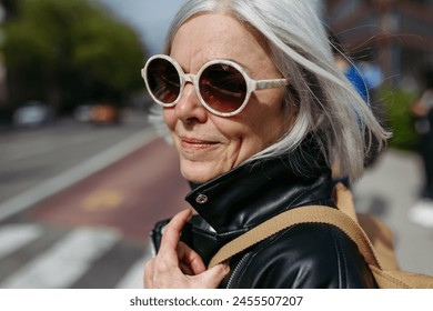 Portrait of stylish mature woman with gray hair on city street. Older woman in sunglasses waiting for public transport. - Powered by Shutterstock