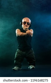 Portrait of stylish midget MC in with headphones and sunglasses posing with microphone.