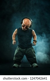 Portrait of stylish midget MC in with headphones and sunglasses posing with microphone.
