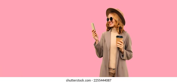 Portrait of stylish smiling woman with smartphone wearing round hat, brown coat on pink background, blank copy space for advertising text - Shutterstock ID 2255444087