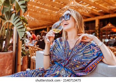 Portrait Of Stylish Young Cheerful Blond Woman Drinking White Wine On A Terrace Bar On A Sunny Summer Day.