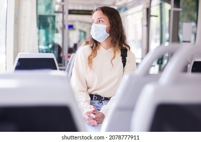 Portrait of stylish young female wearing surgical protective mask during her travel inside tram