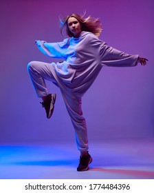 Portrait Of A Stylish Young Girl, Cool Dancing In A Hoodie And With Developing Hair, On A Neon Background.