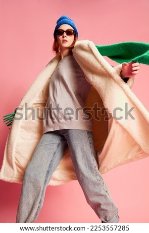 Portrait of stylish young girl in sunglasses, blue hat, green scarf and fur coat posing over pink background. Concept of youth, beauty, winter fashion, lifestyle, emotions, facial expression. Ad