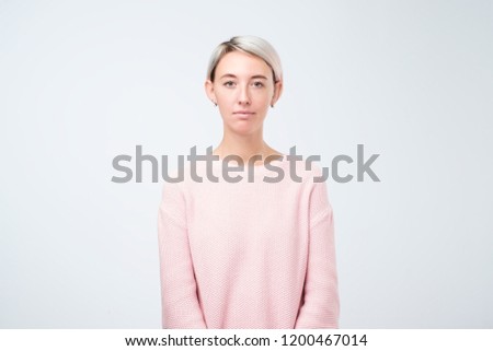 portrait of stylish young pretty woman smiling standing in pink sweater on white studio background. Simple not emotional face