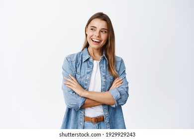 Portrait of stylish young woman with blond hair, cross arms on chest, looking left at empty space for banner and smiling pleased, checking out advertisement, white background - Shutterstock ID 1929929243