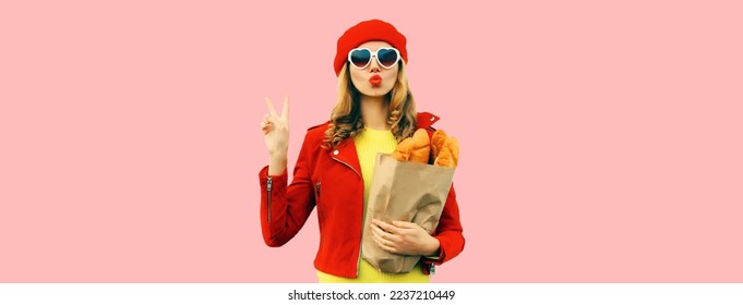 Portrait of stylish young woman blowing her lips sends kiss holding grocery shopping paper bag with long white bread baguette wearing red french beret, heart shaped sunglasses on pink background - Shutterstock ID 2237210449