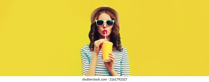 Portrait einer stylischen jungen Frau, die Frischsaft trinkt, mit Sommerstrohhut, Sonnenbrillen und gestreiftem T-Shirt auf gelbem Hintergrund