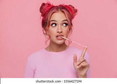 Portrait Of Stylish Young Woman In T-shirt With Colored Hair Stretching Chewing Gum Isolated Over Pink Background