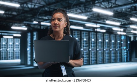 Portrait of Successful African American Female IT Specialist Using Laptop, Standing in Data Center. System Administrator Works on Web Services. Cloud Computing, Server Analytics, Cyber Security - Powered by Shutterstock