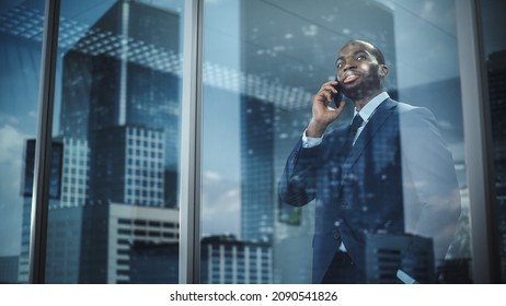 Portrait of Successful African-American Businessman Standing in Office, Making Phone Call to Close the Deal, Looking out of Window. Successful Stock Market Investor Making e-Business. Outside Shot - Powered by Shutterstock