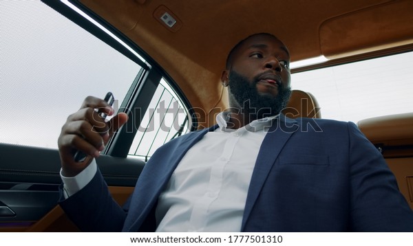 Portrait of successful afro man dancing in luxury\
car. Happy african businessman listening music on mobile phone at\
backseat. Stylish black business man dancing with smartphone in\
hand.