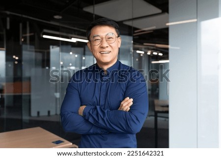 Portrait of successful asian boss inside office, businessman with crossed arms smiling and looking at camera, man in shirt and glasses happy with result of achievement at work.