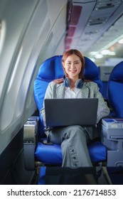 Portrait Of A Successful Asian Business Woman Or Female Entrepreneur In Formal Suit In A Plane Sits In A Business Class Seat And Uses A Computer Laptop During Flight