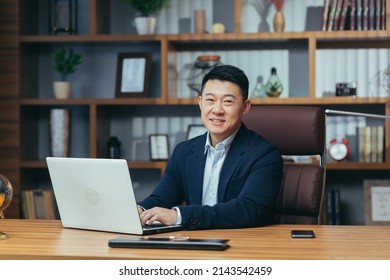 Portrait Of A Successful Asian Businessman, Man Working In The Office Sitting At The Table, Looking At The Camera And Smiling, Happy Banker With Laptop