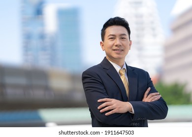 Portrait of successful asian businessman standing with arms crossed standing in front of modern office buildings - Shutterstock ID 1911647503