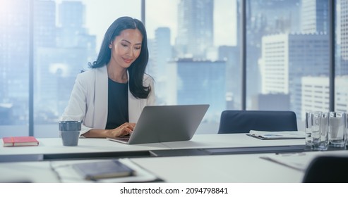 Portrait of Successful Asian Businesswoman Wearing in Stylish Suit Working on Laptop Computer in Big City Office. Powerful CEO Managing Digital e-Commerce Project, Data Analysis, Product Marketing