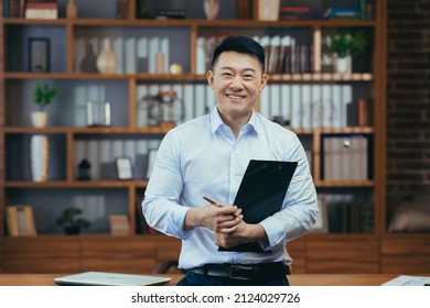 Portrait of a successful Asian teacher, a man in a shirt looking at the camera and smiling, in the classic office of the university director