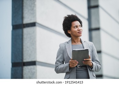 Portrait Of A Successful Black Business Woman Using Digital Tablet During Quick Break In Front A Corporate Building.