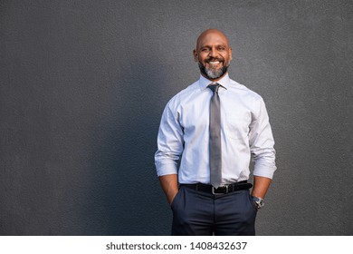 Portrait of successful black businessman standing against grey wall. Smilng senior entrepreneur in formal clothing looking at camera. Mature happy man isolated on grey background with copy space.