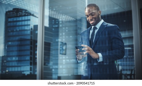 Portrait of Successful Black Businessman Wearing Suit Standing, Using Smartphone Looking out of the Window. Successful African CEO Planning e-Commerce Investment Strategy. From Outside Shot - Shutterstock ID 2090541715