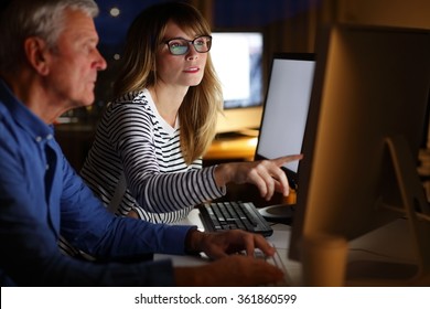 Portrait Of Successful Business Team Working Late Night At Office. Middle Age Professional Woman And Senior Businessman Sitting At Office In Front Computer And Working. 