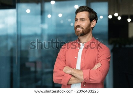 Portrait of a successful businessman inside the office, the man is smiling and looking towards the window, with his arms crossed.