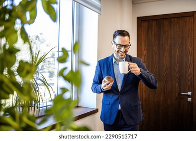 Portrait of successful businessman in the office drinking coffee and eating chocolate donuts.