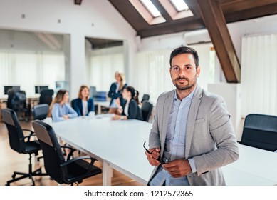 Portrait of successful businessman with people in background at office meeting. - Shutterstock ID 1212572365