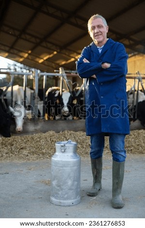 Portrait of successful confident aged man dairy farm owner standing in cowshed outdoors with big can for milk