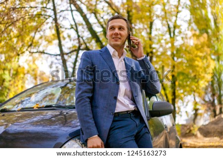 Portrait of successful confident businessman in business suit talking on the phone near the car.