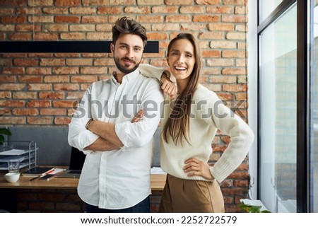 Portrait of successful couple standing at small office. Happy new business partners posing together