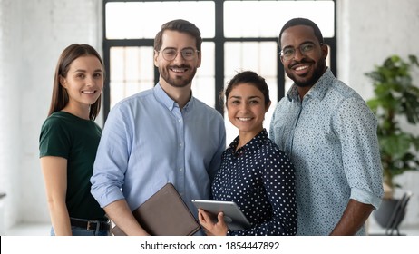 Portrait of successful diverse international business team friendly group of four coworkers capable reliable professional specialists posing at office standing close together smiling looking at camera