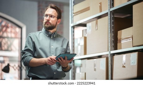 Portrait of a Successful Employee Checking Inventory, Writing in Tablet Computer. Stylish Man Working in a Warehouse Storeroom with Rows of Shelves Full of Packages with Orders Ready for Shipment.