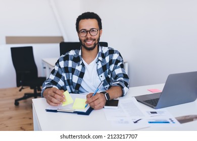 Portrait Of Successful Employer In Optical Spectacles Smiling At Camera During Daytime In Office Interior, Skilled Entrepreneur In Eyewear Posing At Desktop With Digital Netbook For Web Analyzing